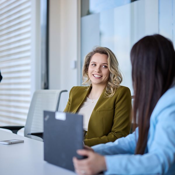 Two ladies sitting down, discussing at an office.